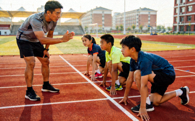 专业田径教练在校园跑道上指导青少年学生进行短跑起跑姿势训练