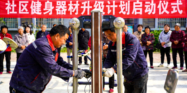 施工人员正在安装新的社区健身器材，周围有升级计划启动仪式的横幅