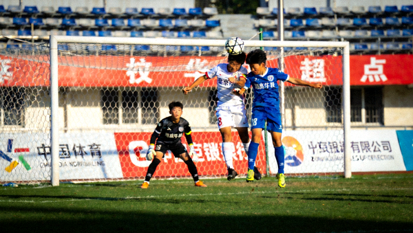 青少年足球锦标赛决赛中球员在门前争顶头球的对抗画面